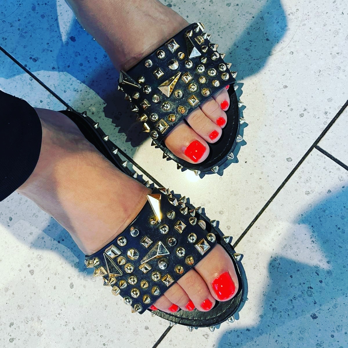 Koraalrode gellak op de tenen, in zwarte sandalen met studs